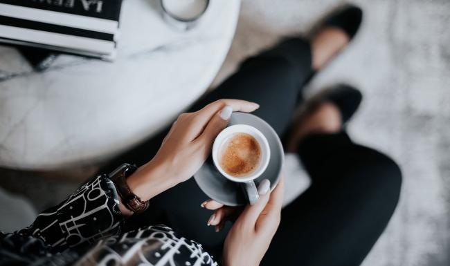 Bustling community with plenty of dining choices business woman sits next to a marble table with books and holds a saucer with a cup of espresso